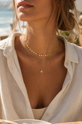 Close-up of a person wearing a gold necklace with a star pendant, outdoors.